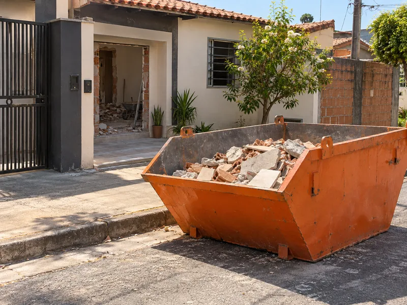 Ilustração de caçamba na calçada de uma casa em reforma, com restos de tijolo e piso ao lado